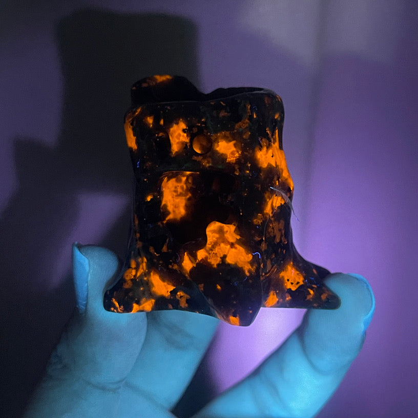 Hand-carved Yooperlite crystal figures with tree-like forms, emitting bright orange fluorescence in UV lighting.