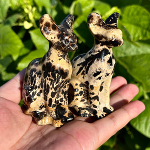 Pair of hand-carved picture jasper cat statues with natural spotted patterns, displayed on a palm.