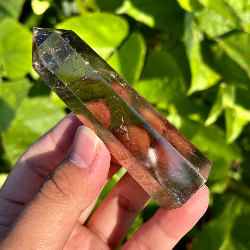 Polished smoky quartz towers held in hand under sunlight, showcasing grounding energy and clarity.