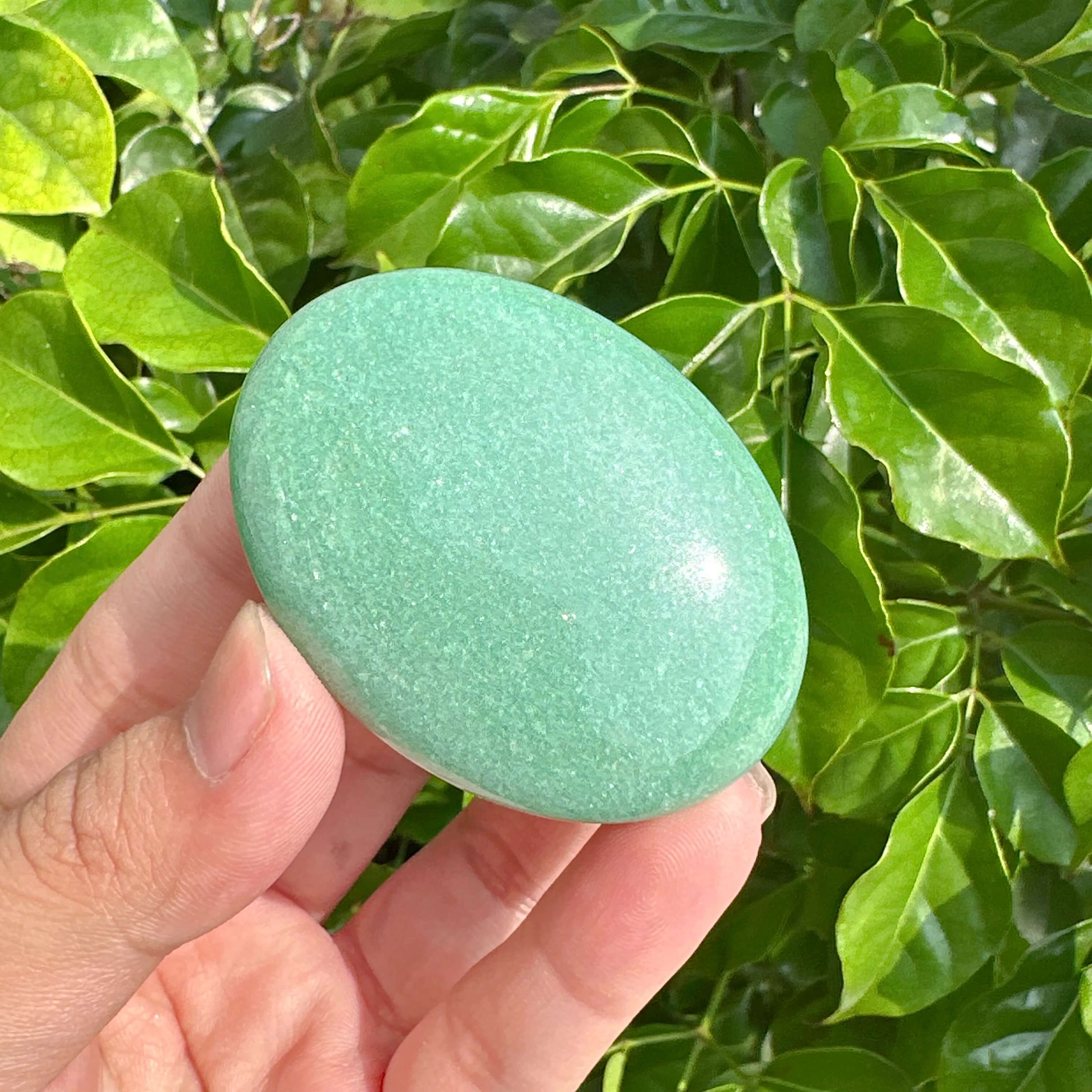 Natural Green Aventurine Palm Stone highlighted against vibrant greenery, offering a calming aura.