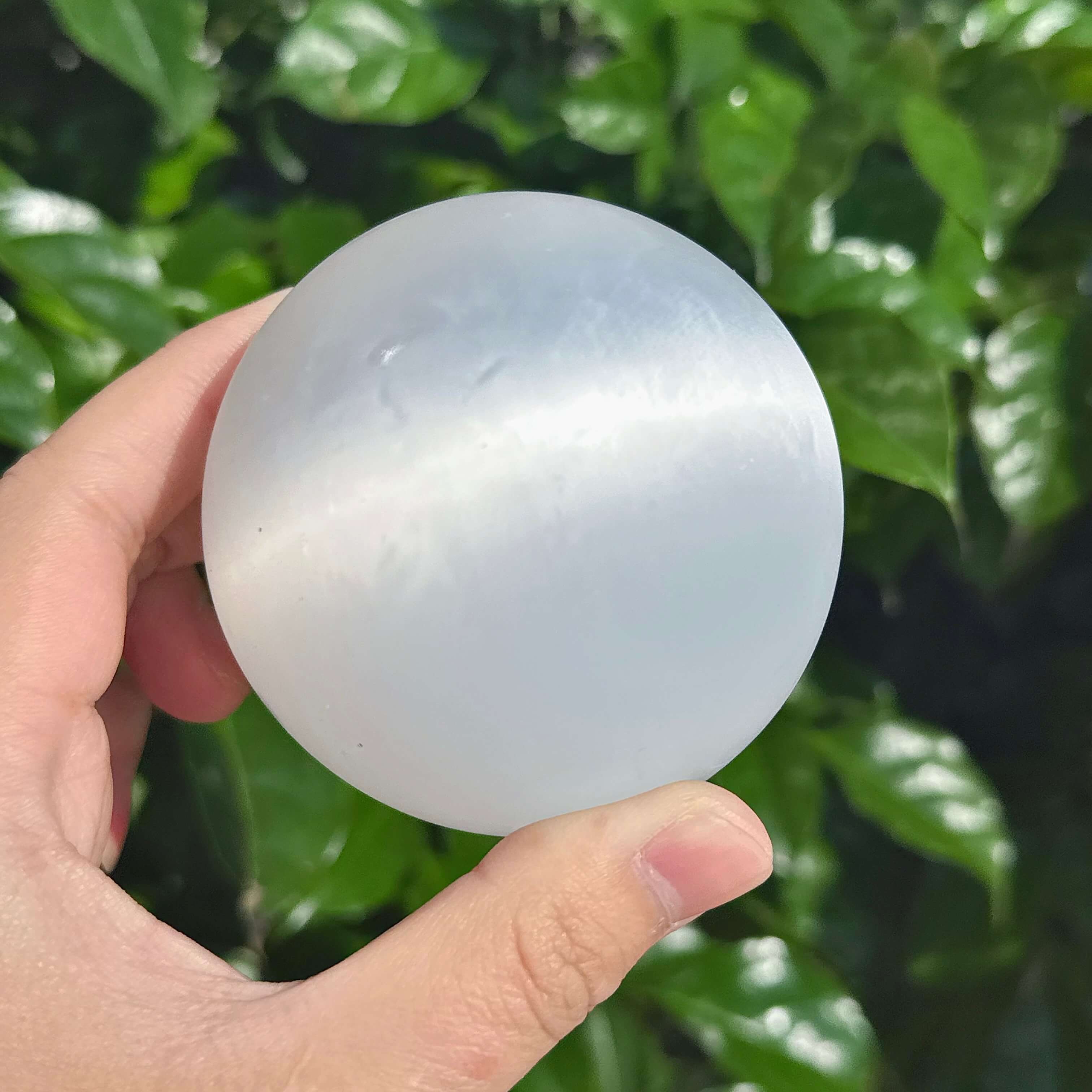 Hand-held selenite sphere with smooth texture, reflecting light and promoting spiritual balance.