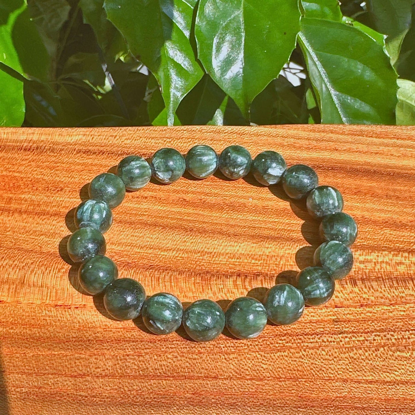 Seraphinite bracelet with green gemstone beads on a wooden surface, showcasing natural healing stones.