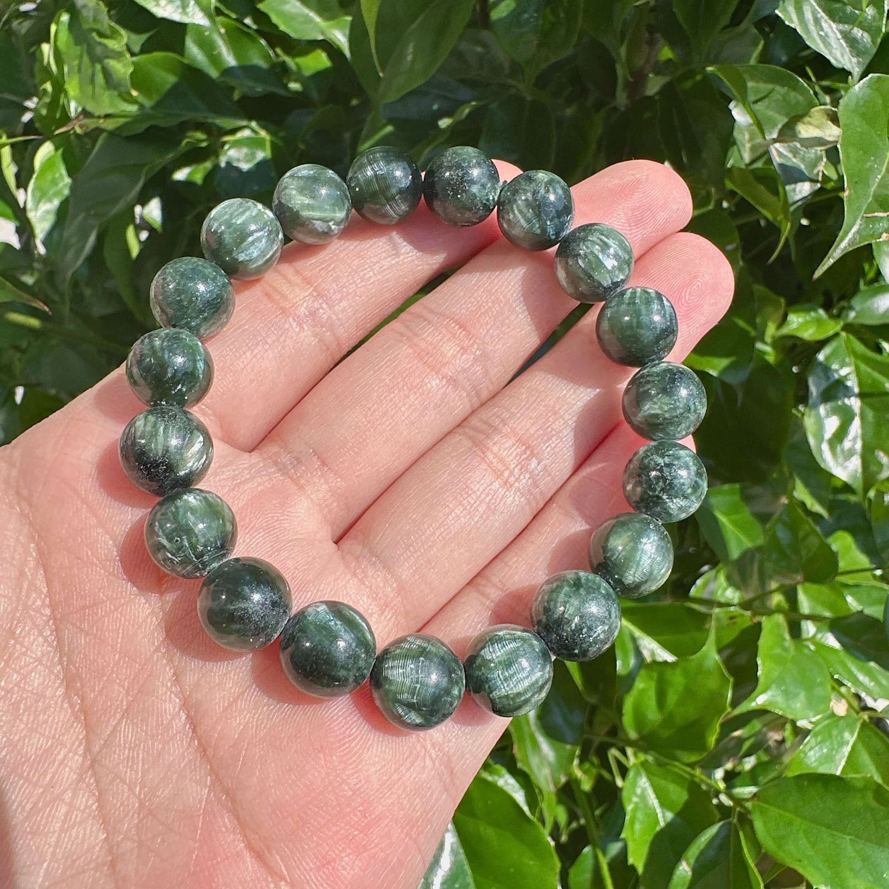 Seraphinite bracelet held in hand with green gemstone beads, ideal for enhancing spiritual energy and personal growth.