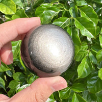 Close-up of a polished Silver Obsidian sphere showing smooth reflective patterns.