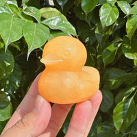 Yellow Calcite Duck Carvings on a wooden surface with a bright background of leaves.